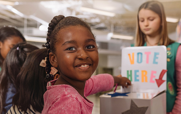 Young Girl Scout putting a ballet in a ballet box, looking at the camera smiling