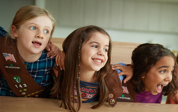 Three Brownie Girl Scouts with their arms around each other smiling at the camera