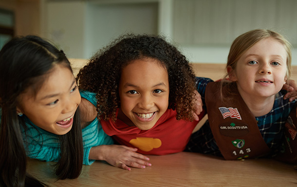Three Brownie Girl Scouts with their arms around each other's shoulders, laughing