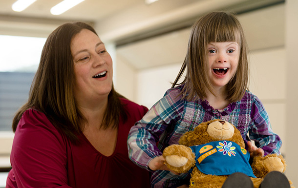  Adult mom with young elementary Girl Scout daisy smiling holding Build a Bear stuffed bear in daisy uniform.